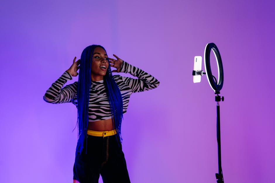 Stylish woman with blue hair poses confidently under vibrant lighting in a studio setting.