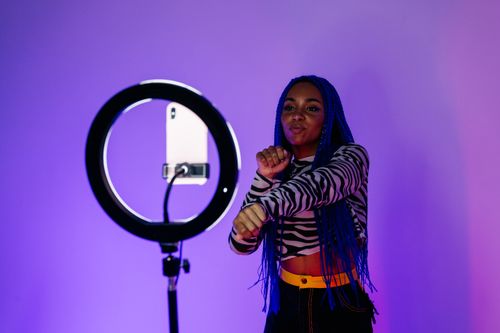 Free Woman with blue hair dancing in a studio, captured with a ring light and purple background. Stock Photo