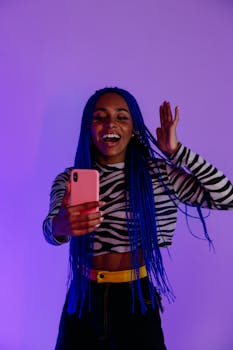 Smiling woman with blue braids taking a selfie, expressing joy against a vivid backdrop.