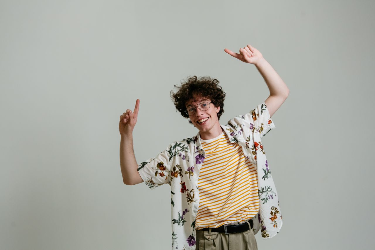cheerful young man with curly hair and glasses smiling and pointing up