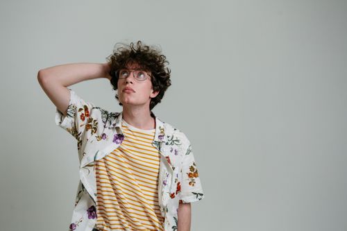 Free A young man with curly hair and glasses thinking in a studio setting. Stock Photo