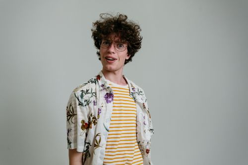 Free A young man with stylish attire and glasses poses indoors, showcasing a playful expression. Stock Photo