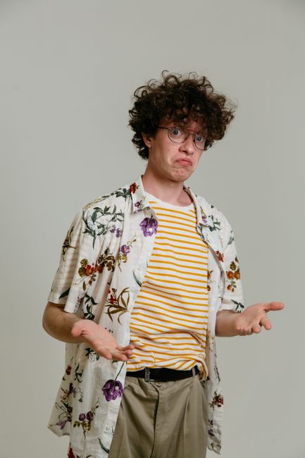 Fotomural Retrato casual de un joven con camisa de flores encogiendo los hombros en interiores con un fondo gris neutro.