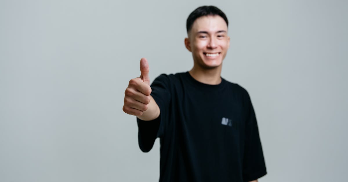 A cheerful young man in a black shirt smiles and gives a thumbs up in a studio setting.