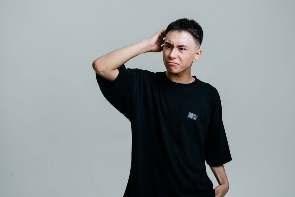 灰色の背景に困惑した表情を浮かべる若い男性のスタジオポートレート。