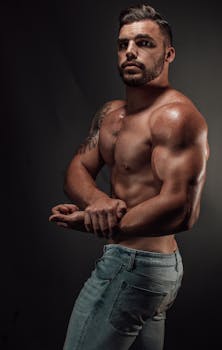 Portrait of a fit, muscular man flexing his arms in a studio setting, wearing denim jeans.