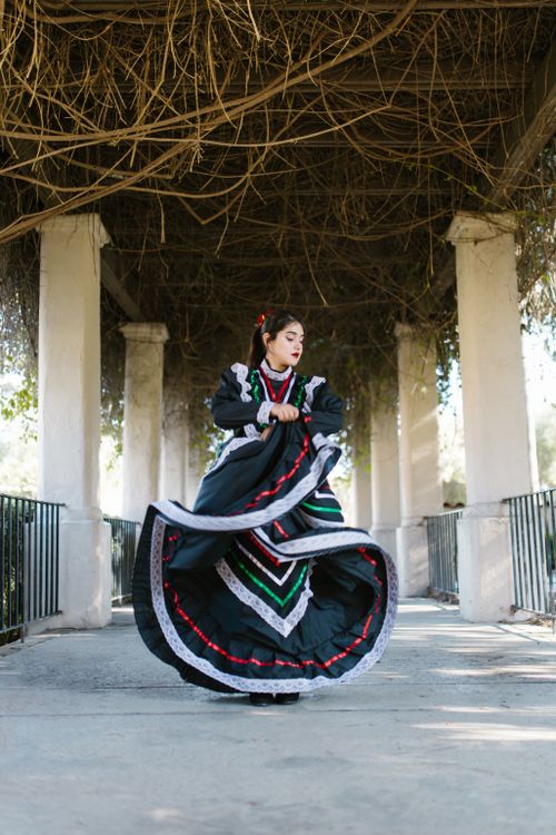 Free A dancer in vibrant traditional Mexican dress performing under a beautiful outdoor arbor. Stock Photo