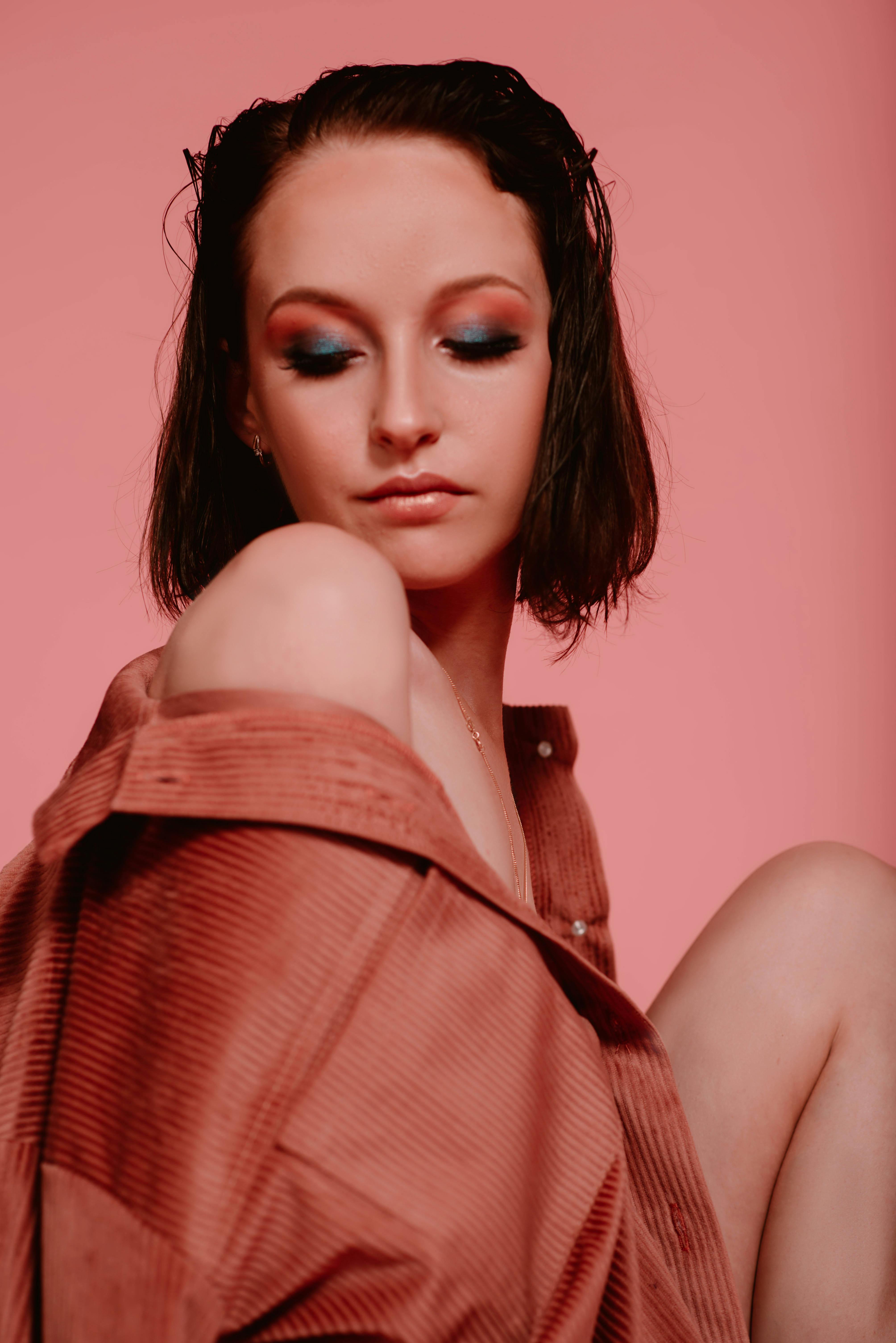 Elegant portrait of a young fashion model posing against a pink background, showcasing stylish makeup and a chic outfit.