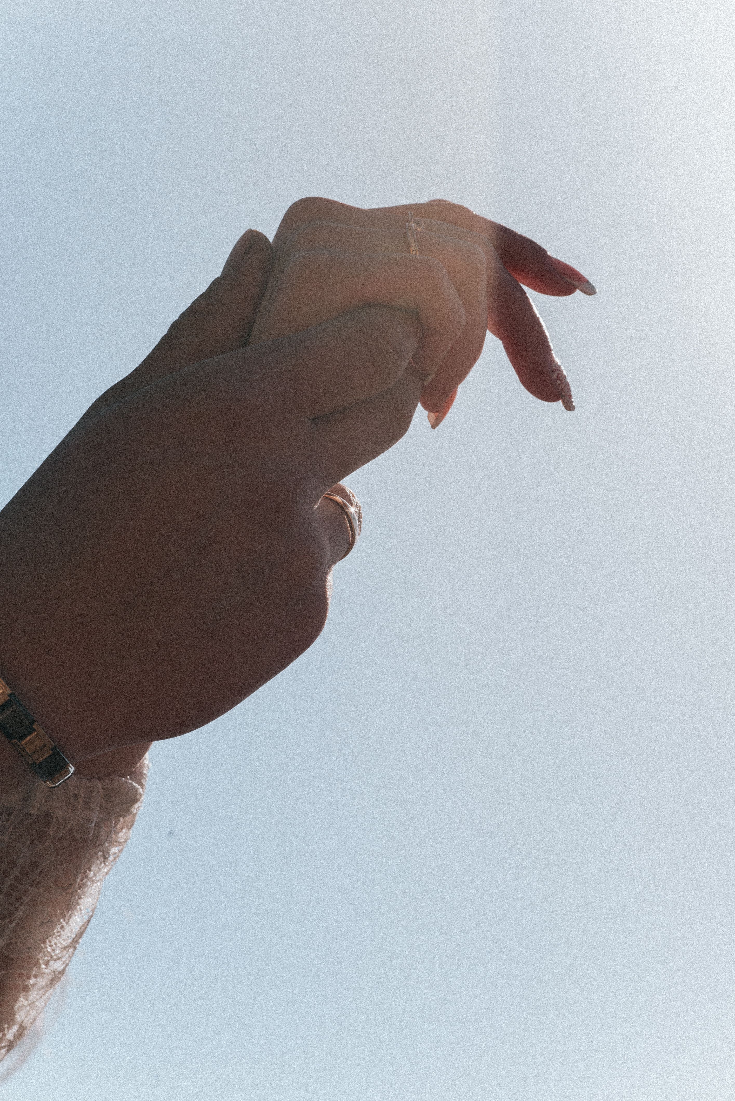 Artistic shot of hands clasped together under a clear blue sky.