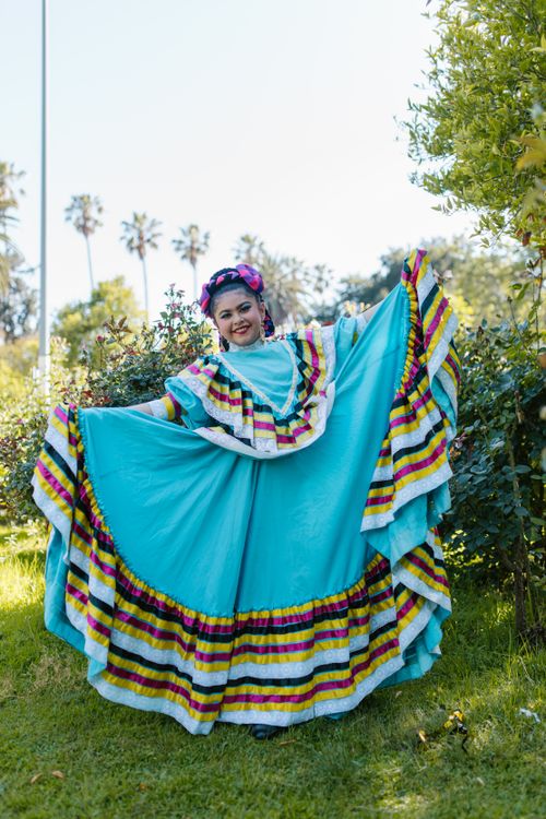 Free A young Hispanic woman in a vibrant traditional dress enjoys a cultural celebration outdoors. Stock Photo