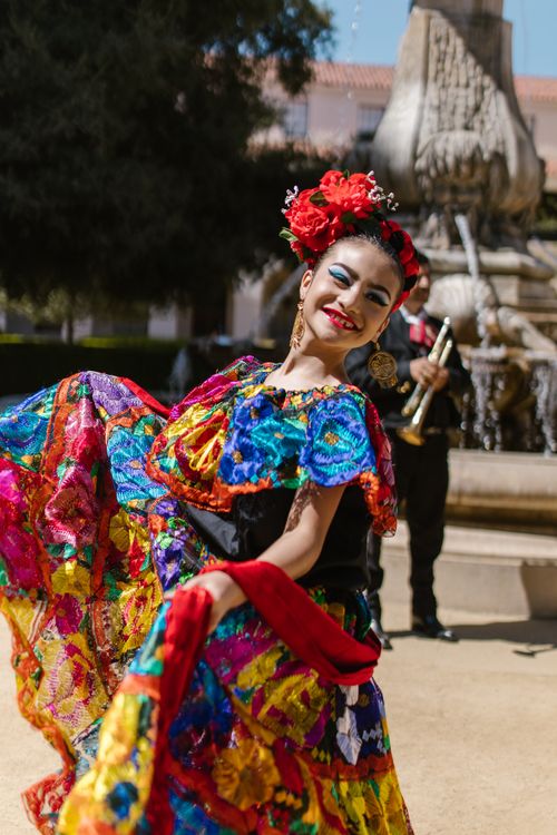 Free A young Hispanic woman in colorful traditional dress dances joyfully at a Mexican festival. Stock Photo