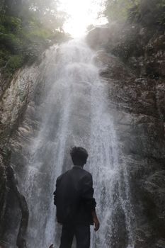 A person standing below a cascade, admiring the waterfall's beauty amidst lush greenery.