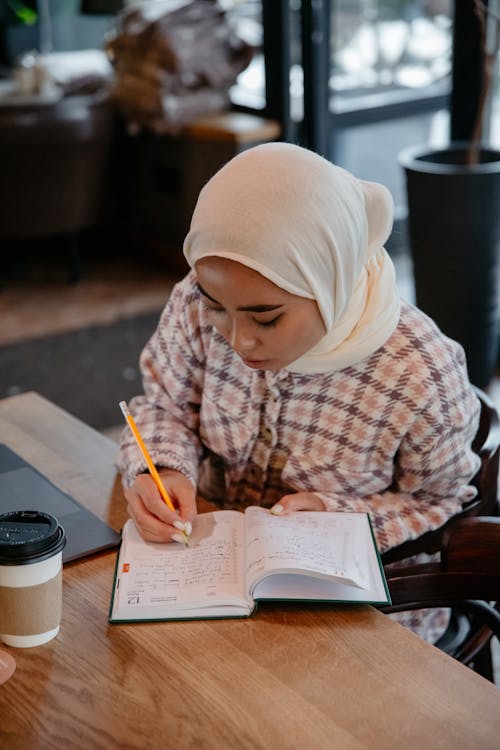 A Woman in White Hijab Holding a Pencil and a Notebook