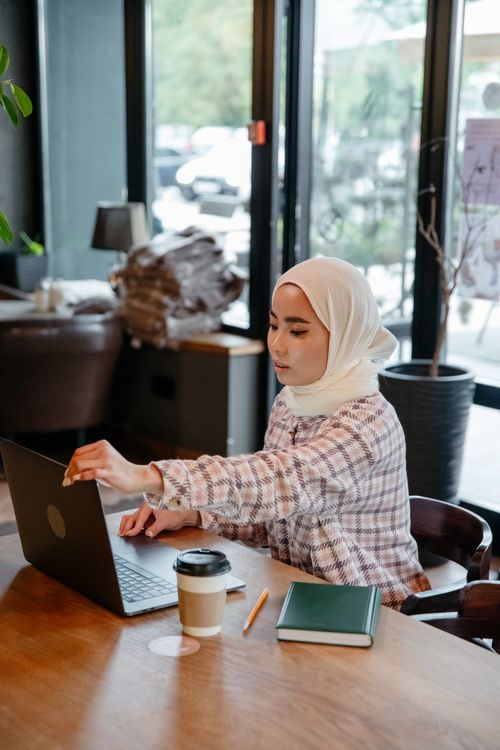 Woman in White Hijab Sitting by the Table Using a Laptop · Free Stock Photo