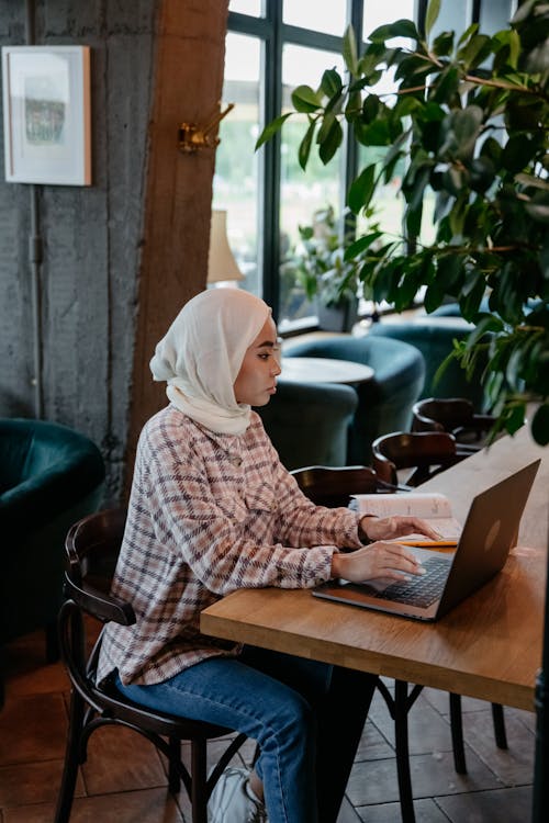 Free Woman in White Hijab Sitting Inside a Shop Using Laptop Stock Photo
