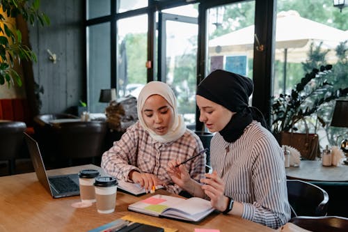 Two Women Sitting Inside a Coffee Shop Sharing Notes and Ideas