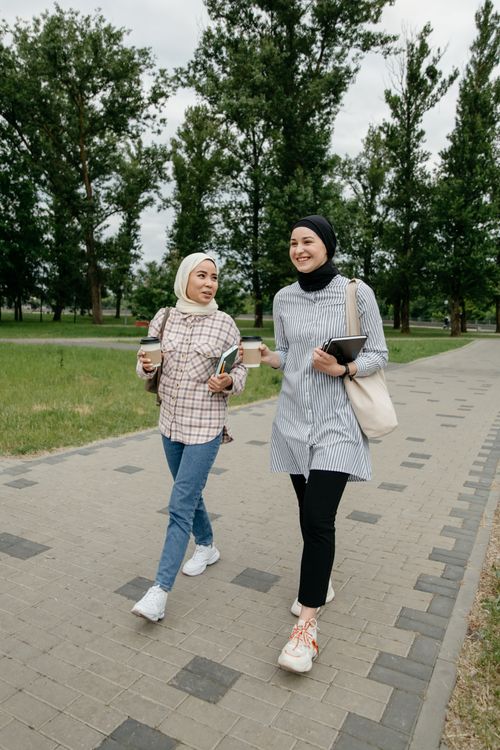 Free Two Muslim women in hijabs walking and chatting leisurely on a park pathway, enjoying friendship Stock Photo