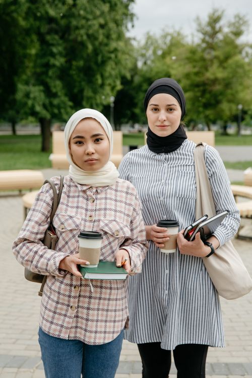 Free Two women in hijabs holding coffee cups and notebooks, standing outdoors. Stock Photo