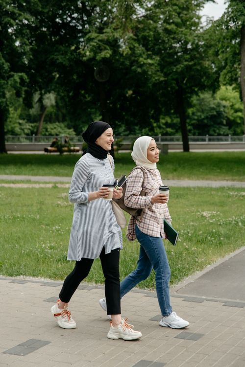 Free Two young women in hijabs strolling in a city park, enjoying coffee and conversation. Stock Photo