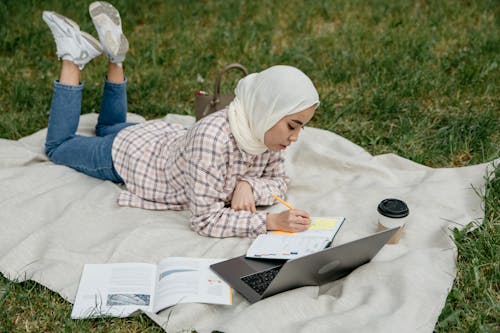 Woman Taking Notes Lying on a Blanket in the Park