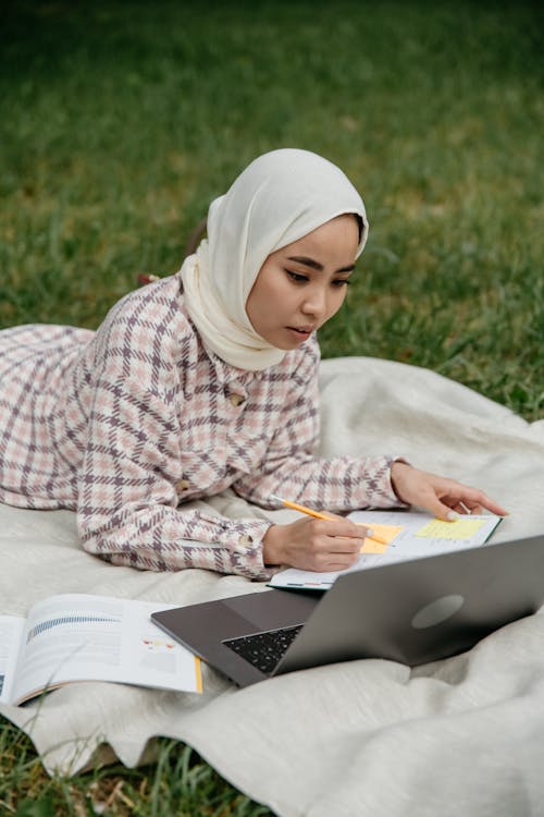 A Woman in White Hijab Writing on a Notebook