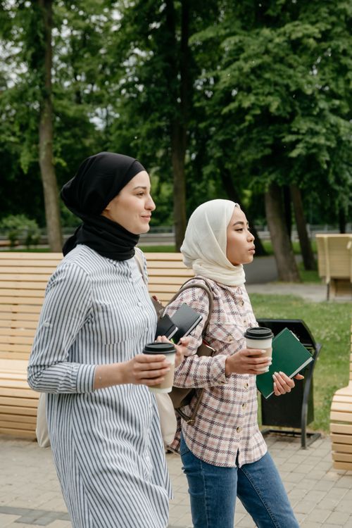 Free Two women in hijabs walking with coffee cups in a park setting. Stock Photo