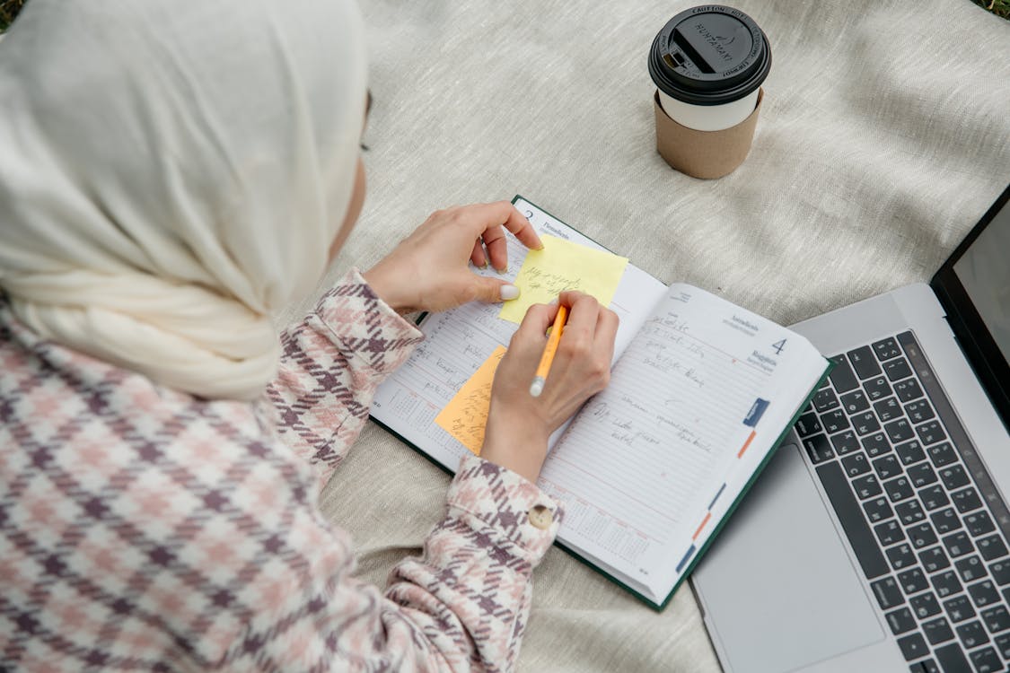 Overhead Shot of a Woman Writing on a Yellow Sticky Note