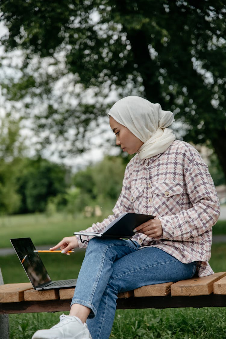 Woman Working On A Laptop Sitting On A Park Bench