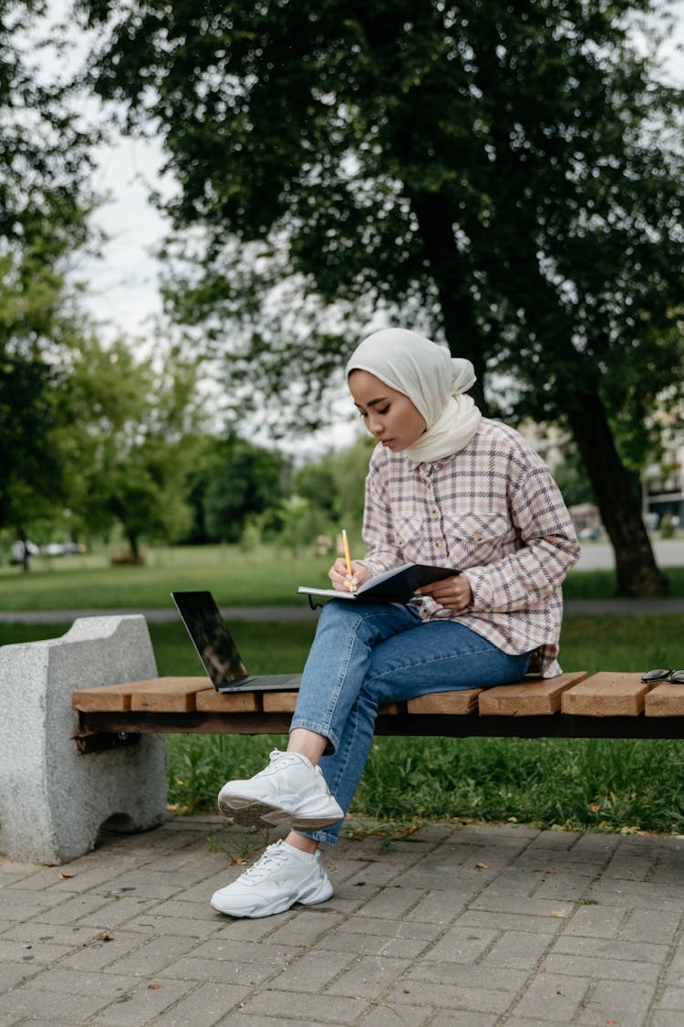 Woman Filling Out A Planner Sitting On A Park Bench