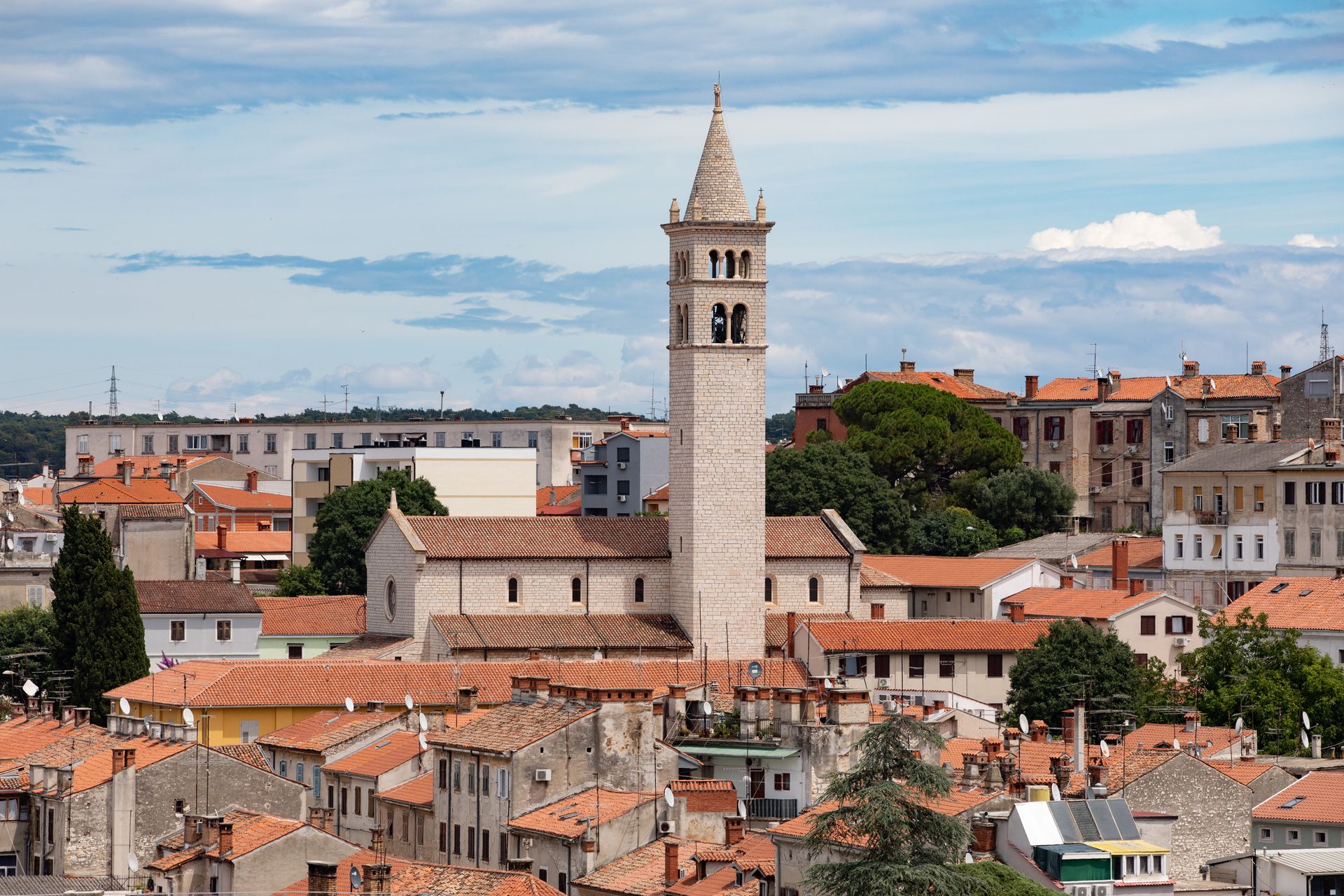 Aerial view of historic church tower amidst Pula, Croatia's cityscape on a sunny day.