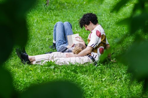 Free Couple enjoying a peaceful afternoon reading in a grassy park setting. Stock Photo