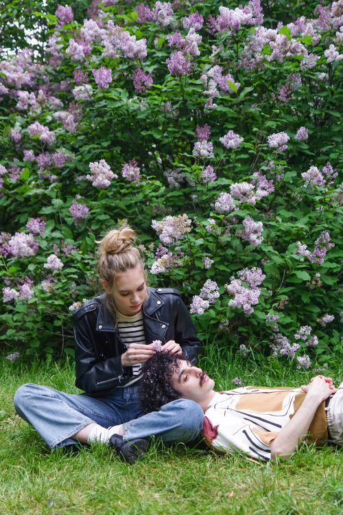 Free Young couple enjoying a serene moment surrounded by lilac flowers in a lush garden. Stock Photo