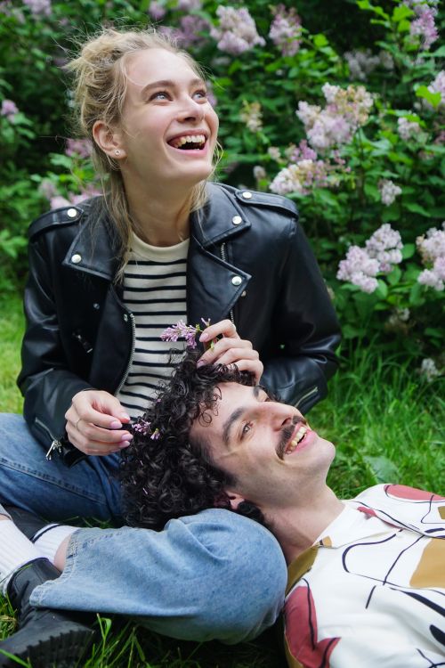 Free A joyful couple in casual attire surrounded by blooming lilacs outdoors. Stock Photo