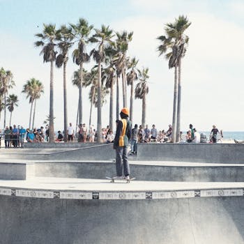 A skateboarder performing at Venice Beach skate park in Los Angeles, surrounded by palm trees and onlookers.
