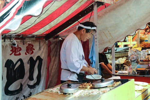 Man in White Robe Cooking on Market Stall