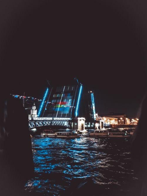 Free Vibrant night scene of an illuminated drawbridge raising over a dark, rippling river. Stock Photo