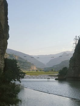 Dramatic view of a bridge spanning a tranquil lake amidst towering cliffs and mountains in Dagestan, Russia.