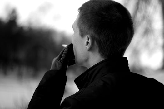 Black and white image of a man smoking outdoors, capturing a pensive moment.