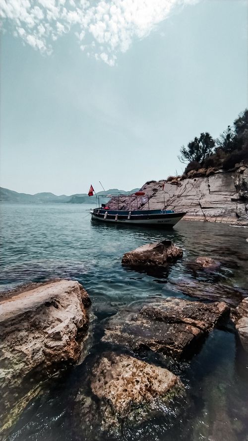 Free A serene beach scene featuring a moored boat by rocky shores under a clear blue sky. Stock Photo