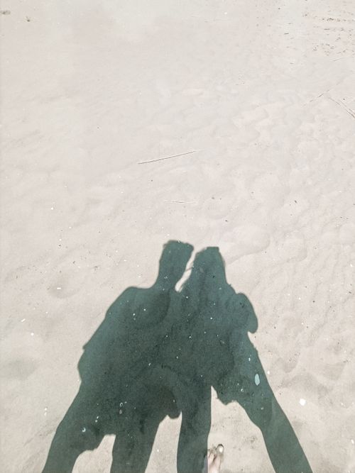 Free Silhouetted shadows of two people on a sunlit sandy beach with no visible landmarks. Stock Photo