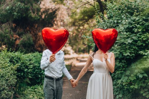 Free A couple holding red heart-shaped balloons outdoors, symbolizing love and romance. Stock Photo