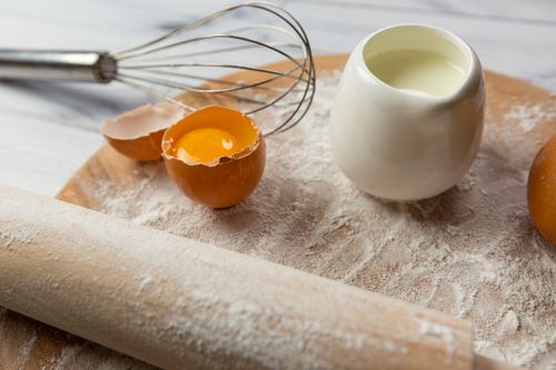 Free Close-up of baking ingredients including egg yolk, flour, and milk on a wooden surface. Stock Photo
