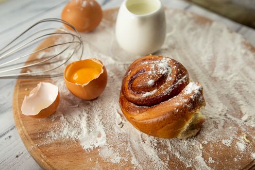 Freshly baked cinnamon roll with egg and milk on a floured board, perfect for breakfast inspiration.
