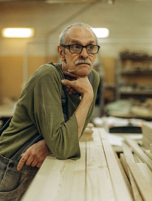 Free Elderly man with glasses thinking in a woodworking workshop indoors. Stock Photo