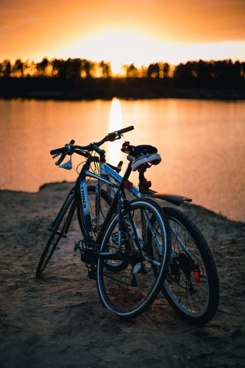 Free Two bicycles resting by a serene lake at sunset, creating a romantic and peaceful setting. Stock Photo