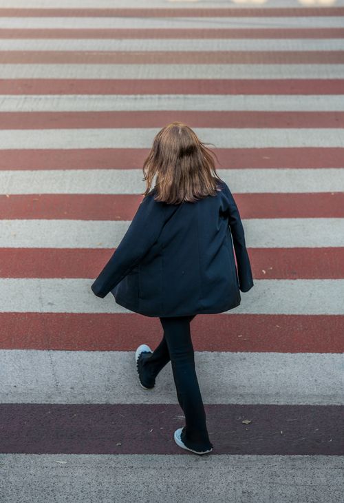 Free Rear view of a person crossing a red and white striped crosswalk outdoors. Stock Photo