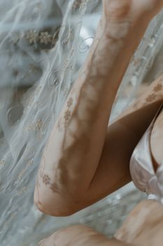 Close-up of an arm with intricate floral shadows on a delicate lace backdrop.