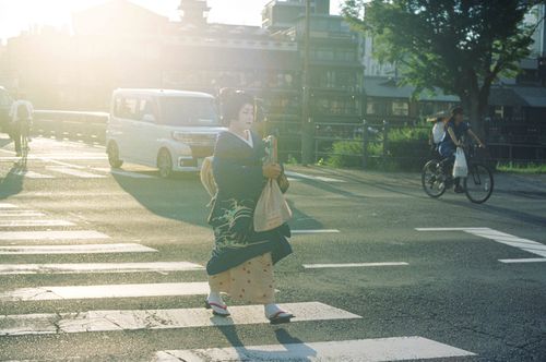 Free Graceful geisha crossing a Kyoto street during sunset, encapsulating traditional Japanese culture in a modern setting. Stock Photo