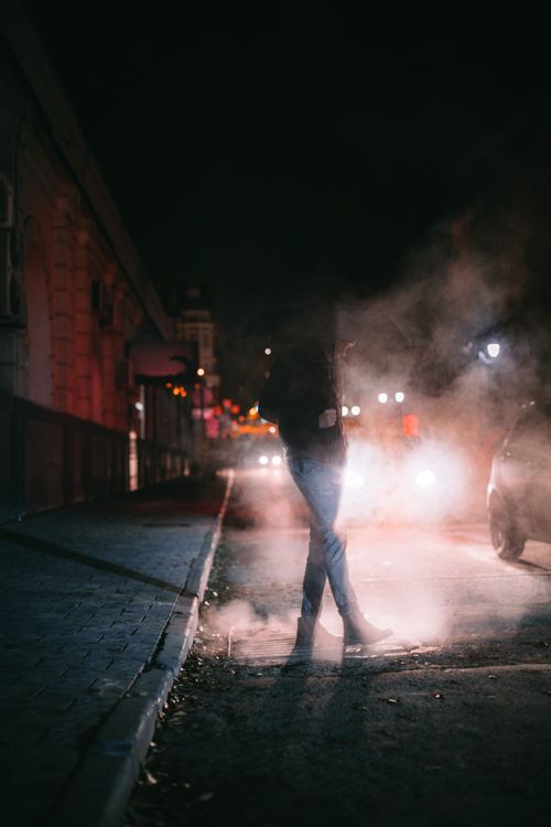 Free A silhouetted person walks through steam on a city street at night, creating a moody ambiance. Stock Photo