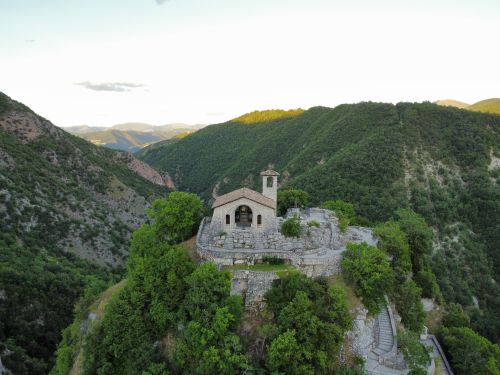 Free A stunning aerial view of a mountain church surrounded by lush greenery and distant peaks. Stock Photo